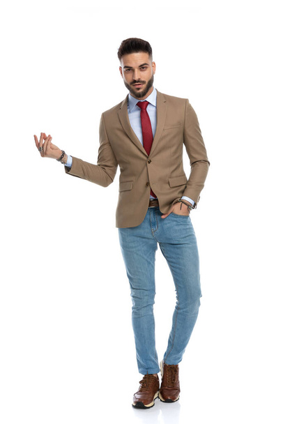 unshaved smart casual model holding hand in pocket and snapping fingers with the other hand while walking on white background in studio - Photo, image