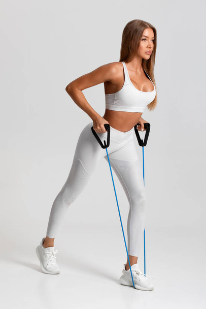Mujer fitness haciendo ejercicio con banda de resistencia sobre fondo gris. Ejercicios de chica atlética con expansor - Foto, Imagen