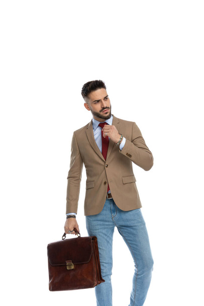 セクシーな髭を生やした男とスーツケースを見ながら横になり赤いネクタイを固定しながらポージングで白い背景にスタジオ - 写真・画像