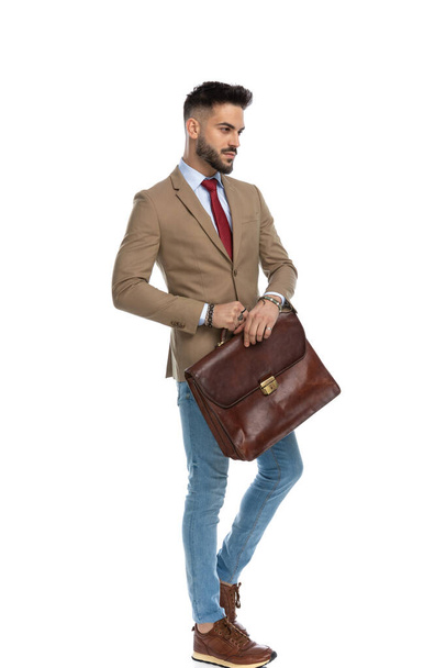 sexy unshaved guy with suitcase looking to side and posing in front of white background in studio - Photo, Image
