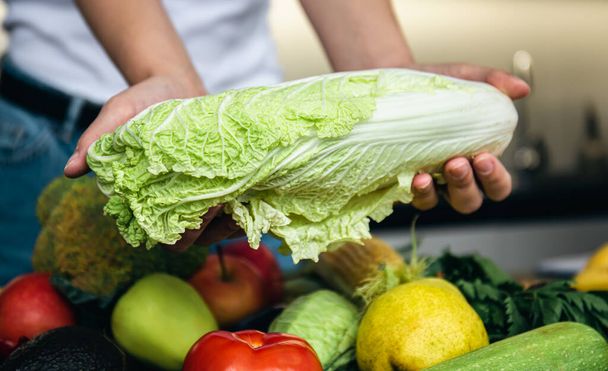 Close-up, cabbage in a womans hand on the kitchen table among vegetables, the concept of cooking. - Photo, Image
