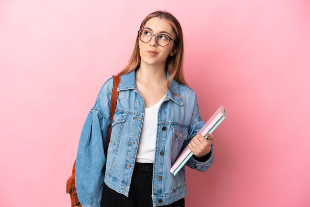 Νεαρή καυκάσια φοιτήτρια απομονωμένη σε ροζ φόντο και κοιτάζει ψηλά - Φωτογραφία, εικόνα