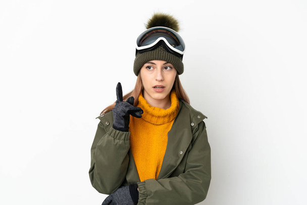 Esquiador mujer caucásica con gafas de snowboard aisladas sobre fondo blanco pensando en una idea apuntando con el dedo hacia arriba - Foto, imagen