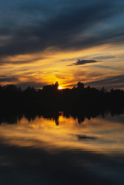 Atmospheric sunset behind trees and reflection in water. - Photo, image