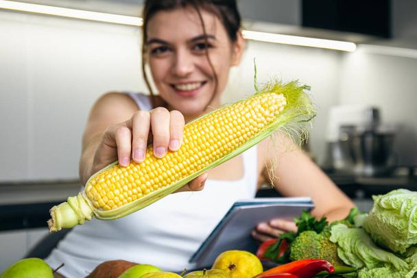 Una joven en la cocina con un cuaderno y verduras, el concepto de cocina, dieta y salud. - Foto, imagen