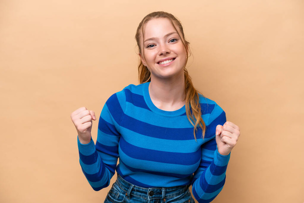 Young caucasian woman isolated on beige background celebrating a victory in winner position - Foto, afbeelding