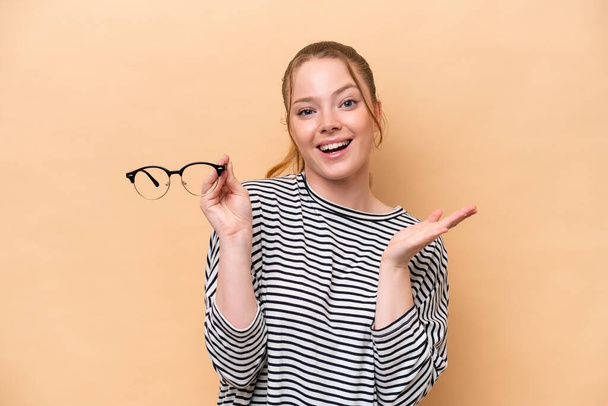 Young caucasian girl with glasses isolated on beige background with shocked facial expression - Photo, Image