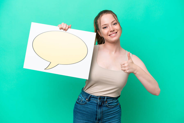 Young caucasian woman isolated on green background holding a placard with speech bubble icon with thumb up - Valokuva, kuva