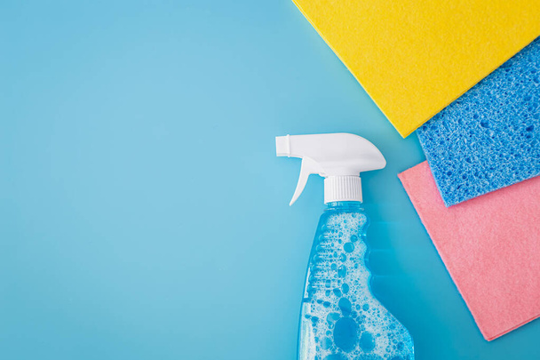 Cleaning spray bottle and colored rags on blue background. Flat lay, top view. House cleaning service and housekeeping concept. - Fotografie, Obrázek
