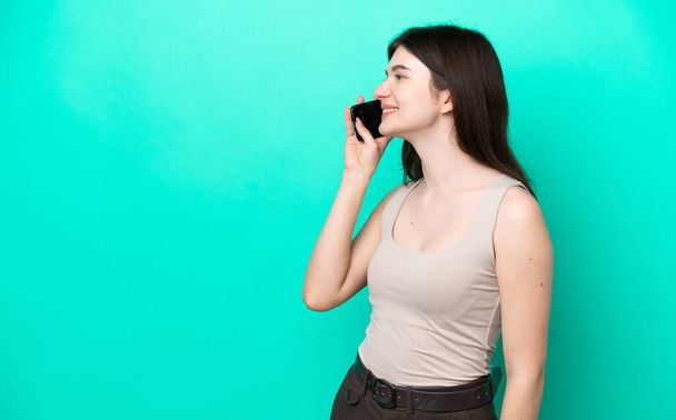 Joven mujer rusa aislada sobre fondo verde manteniendo una conversación con el teléfono móvil con alguien - Foto, imagen