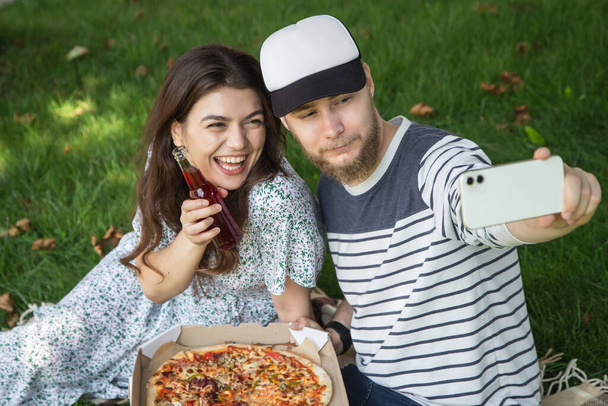 Молодий чоловік і жінка приймають селфі з піцою на пікніку, на відкритому повітрі
. - Фото, зображення