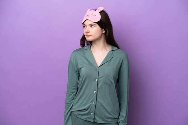 若いですロシア人女性でパジャマで隔離された紫色の背景を見て側 - 写真・画像