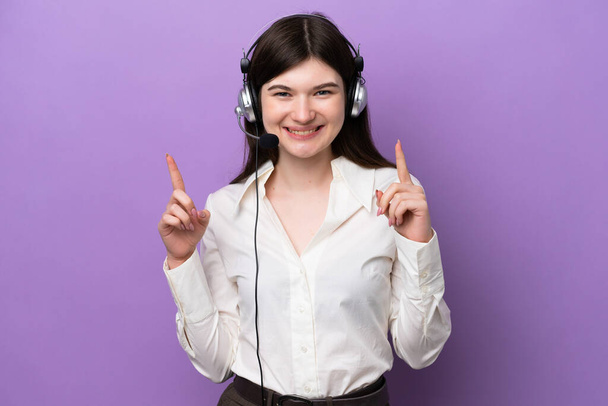 Telemarketer Russian woman working with a headset isolated on purple background pointing up a great idea - Φωτογραφία, εικόνα
