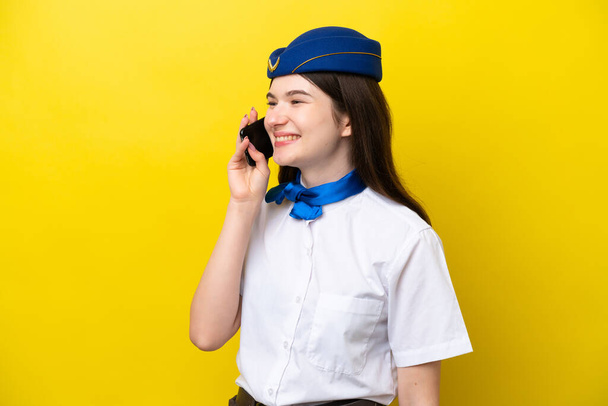 Flugbegleiterin russische Frau isoliert auf gelbem Hintergrund hält ein Gespräch mit dem Mobiltelefon - Foto, Bild