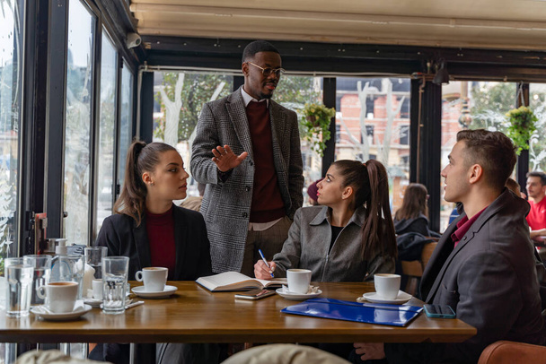 Група багаторасових бізнесменів диктує свої бізнес-плани та ідеї, сидячи в кафе
 - Фото, зображення