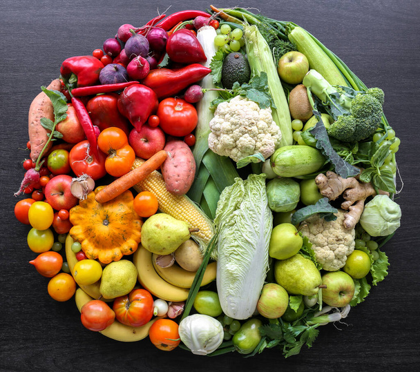 Verschiedenes Gemüse und Obst in einem Kreis auf dunklem Hintergrund ausgebreitet, Draufsicht. - Foto, Bild