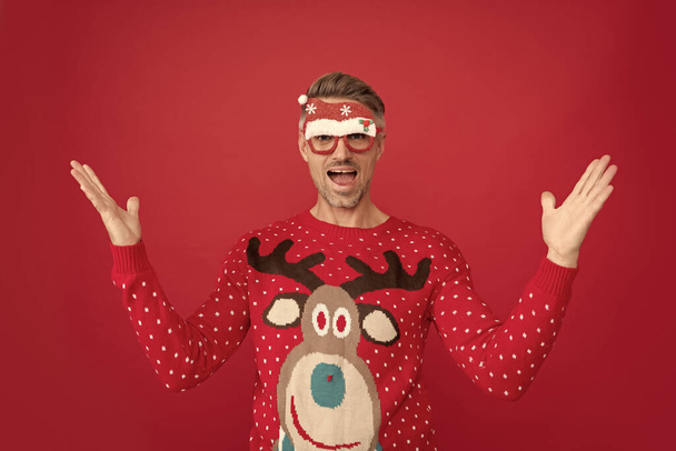 verblüffter Mann in Winterpullover und Party-Weihnachtsmann-Brille. Weihnachtsmann auf rotem Hintergrund. Frohes neues Jahr. Frohe Weihnachten. - Foto, Bild