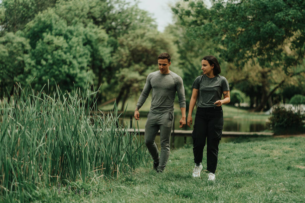 Hermosa pareja deportiva caminando en el parque y buscando algo en el suelo cerca del lago - Foto, imagen