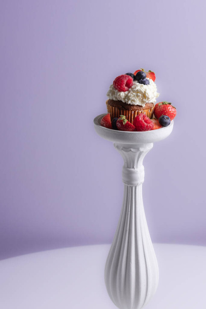 Beautiful muffin with delicious vegan cream, fresh berries on a decorative white pad . Place for your text. Sweet concept. Excellent image for dessert banners and advertisements. Desert background.  - 写真・画像