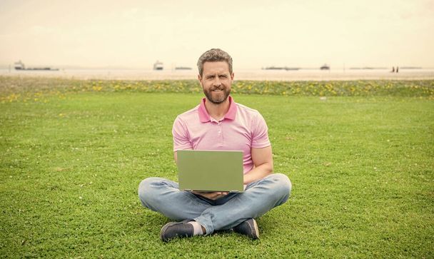 gelukkig zakenman met behulp van laptop voor bloggen op groen gras, freelancer. - Foto, afbeelding