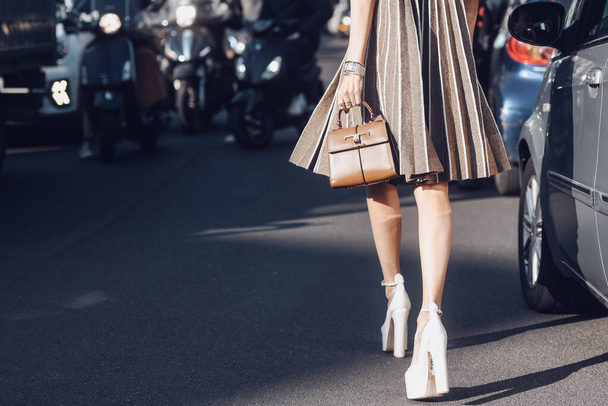 Milan, Itálie - únor, 25: Pouliční styl, žena v béžových a hnědých akordeonových krátkých šatech, hnědá lesklá kožená kabelka, bílá lakovaná kožená podešev vysoké podpatky obuv. - Fotografie, Obrázek