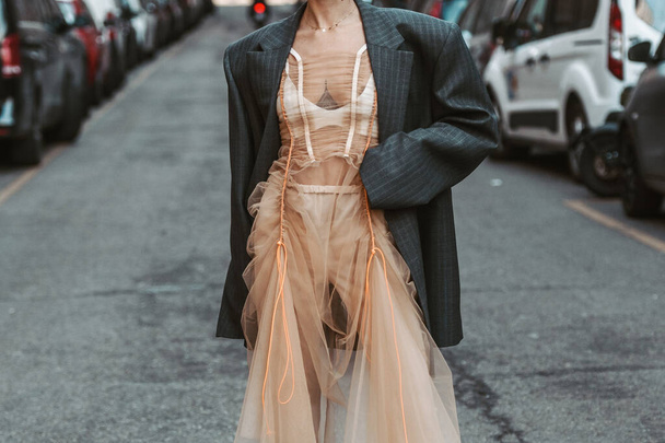 Milan, Italy - February, 25: Street style, woman wearing orange tulle shoulder-off, a dark gray striped oversized blazer jacket, high waist flared suit pants, leather strappy heels sandals. - Foto, Imagen