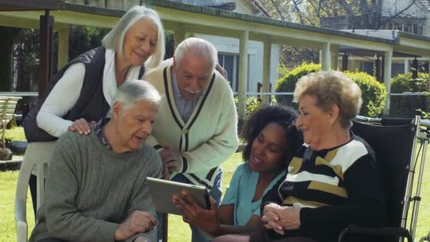 Groep bejaarde gepensioneerden in de tuin glimlachend met tablet. - Video