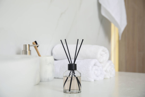 Aromatic reed air freshener, toiletries and towels on white countertop in bathroom - Foto, Imagem