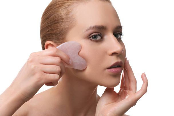Beautiful young woman doing facial massage with gua sha tool on white background, closeup - 写真・画像
