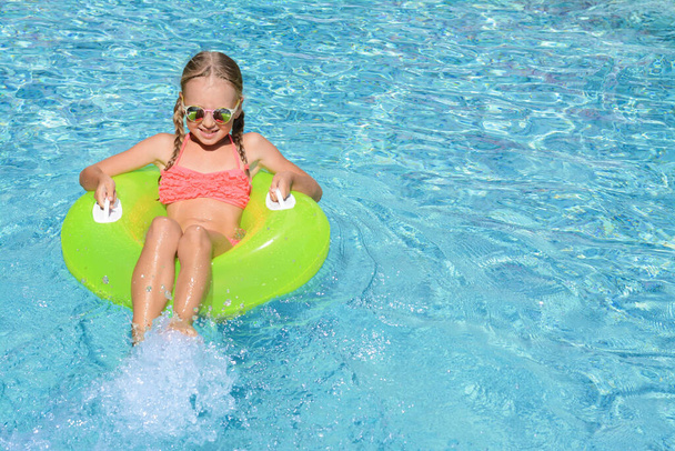 Cute little girl with inflatable ring in pool on sunny day. space for text - Foto, afbeelding