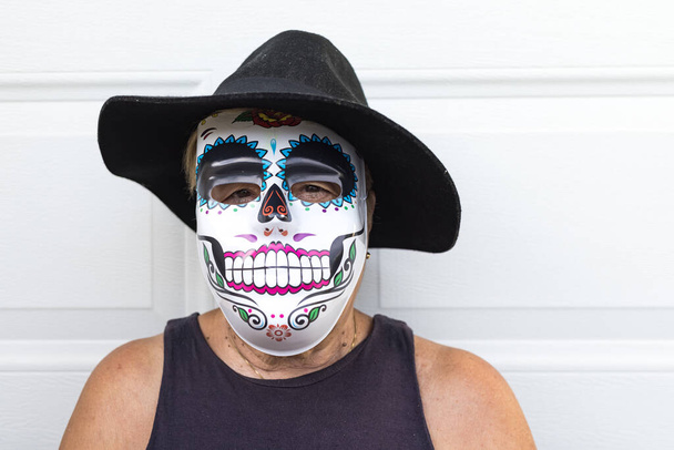 Portrait of an elderly lady with a catrina mask and hat, celebrating Halloween and All Souls' Day, on a white background. Celebration, costume, party and mask concept. - Photo, Image