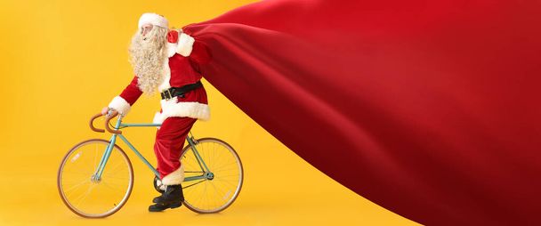 Санта Клаус з великою сумкою їздить на велосипеді на жовтому тлі. Прапор для дизайну - Фото, зображення