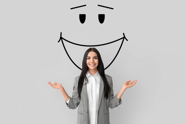 Schöne junge Geschäftsfrau und gezeichnetes Lächeln auf grauem Hintergrund - Foto, Bild