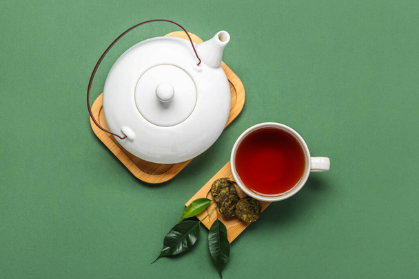 Boards with dry pressed puer tea, cup and teapot on green background - Photo, Image