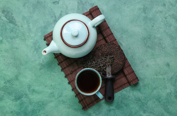 Bamboo mat with dry pressed puer tea, knife, cup and teapot on grunge background - Фото, зображення
