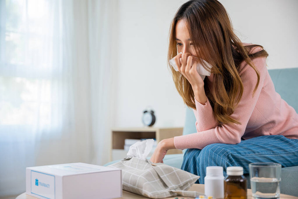 Sick woman. Beautiful female health problem blowing nose use pharmacy kit box delivery service from hospital, delivery pharmacy concept, Asian young girl cold sick she sneeze with tissue paper on sofa - Photo, Image