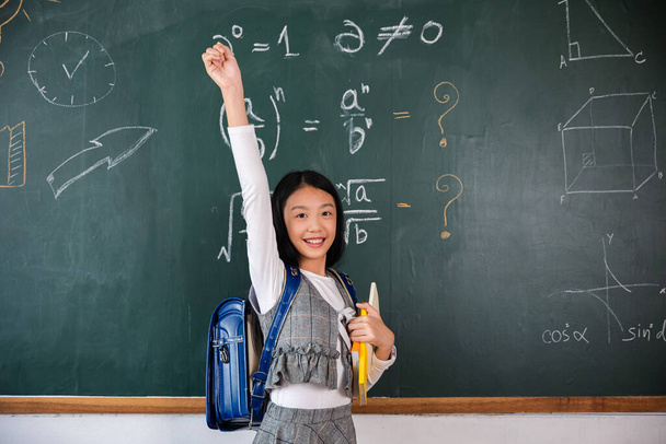 Education Back to school. Asian school girl in uniform on classroom raised arms to successful finished homework, primary child is standing front of class in school raised hands in win position - Fotoğraf, Görsel