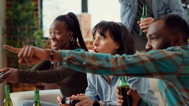 Monipuolinen ihmiset käyttävät konsolia pelata videopelejä, hauskaa online-pelaamista haaste sosiaalinen kokoontuminen. Nautin pelikilpailusta televisiossa ja oluen juomisesta. Kämmentietokone. - Valokuva, kuva
