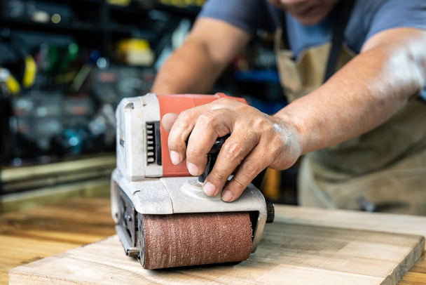 Tischler, der mit Bandschleifer in Werkstatt, Heimwerker und Holzbearbeitungskonzept auf Holz poliert. Selektiver Fokus - Foto, Bild
