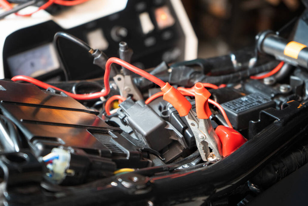 Laden der Motorradbatterie in der Garage, selektiver Fokus auf Alligator-Clip, Konzept der Motorradwartung und -reparatur. - Foto, Bild