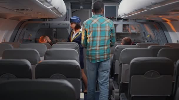 Kadın uçuş görevlisi uçakta yolcularla konuşuyor, uçak biletlerinde turistlere biniyor. Ekonomi sınıfında uluslararası havayolları ile seyahat eden insanlarla sohbet etmek. - Video, Çekim