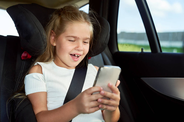 Little caucasian girl using mobile phone in the car  - Photo, Image