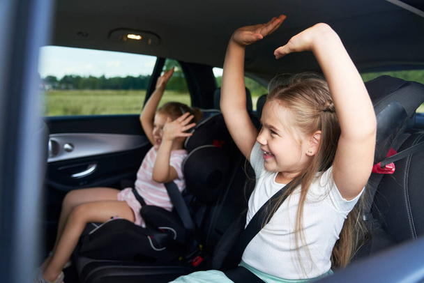 Two caucasian female children riding in the car in the back seat and dancing - Valokuva, kuva