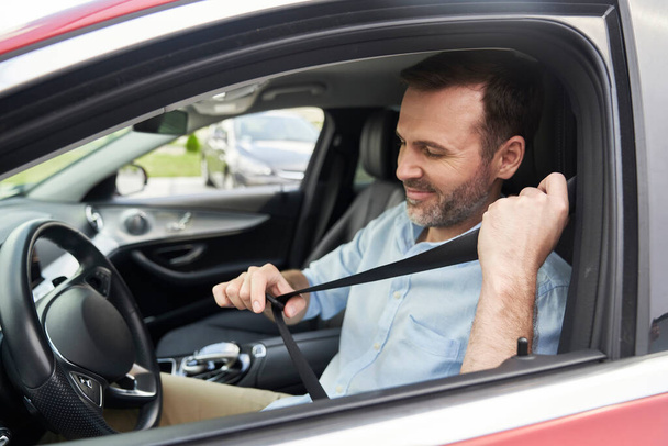 Кавказький чоловік середнього віку застібає ремені безпеки в машині.  - Фото, зображення