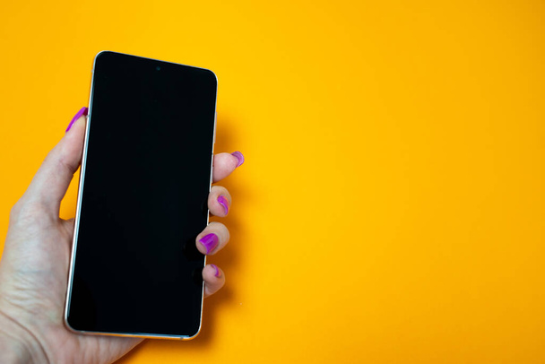 woman hand with nails manicure holding smartphone with blank black screen on yellow background, place, space for text, insert picture, modern technology, connection with internet, wi-fi, messaging  - Fotó, kép