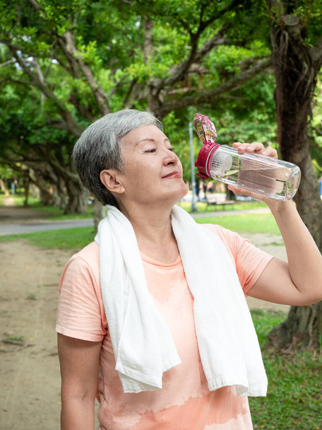 Muotokuva 60-luvun vanhempi aikuinen vanhusten Aasian nainen hymyilee seisoo ja tilalla pullotettua vettä urheilun jälkeen ja nauttia luonnon kanssa raitista ilmaa puistossa. - Valokuva, kuva