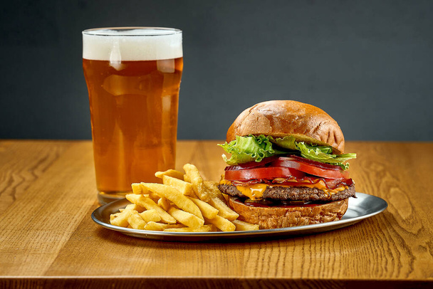 A big juicy burger with vegetables and a glass of beer. Close-up, selective focus - Photo, image