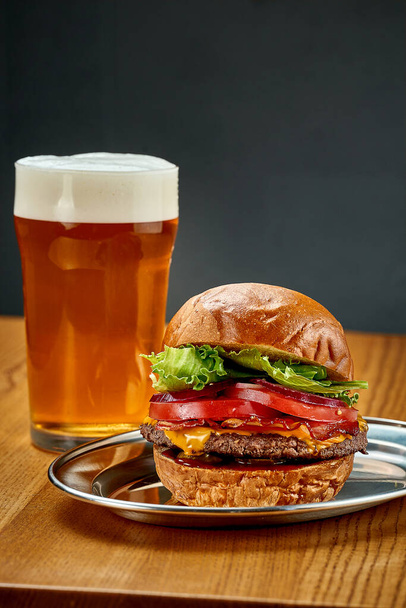 A big juicy burger with vegetables and a glass of beer. Close-up, selective focus - Foto, imagen