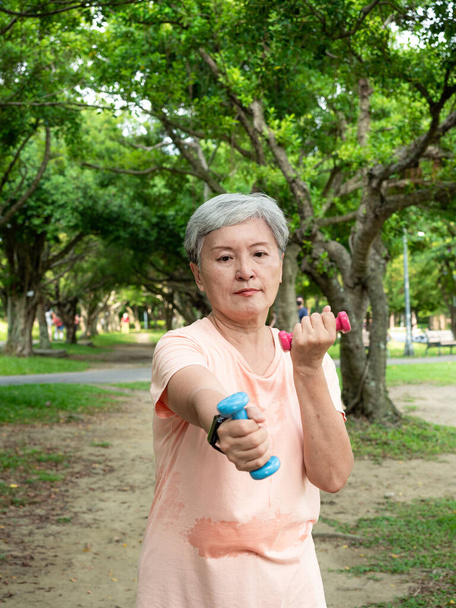 大人のアジア人女性の肖像60年代スポーツ服を着て腕の仕事をし、公園の屋外で健康のためのリラクゼーションとダンベル運動を持ち上げる. - 写真・画像