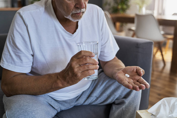 Senior caucasian man taking pill and holding glass of water - Fotó, kép